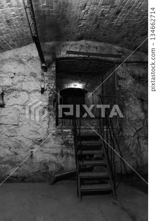 Dark empty underground basement scene with rough stone walls and rusty stairway 134662714