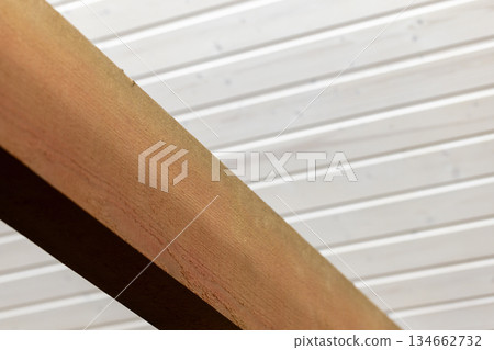 Rough natural wooden beam is under white ceilinfg made of planks 134662732