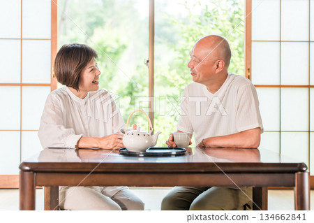 一對老年夫婦在日式房間喝茶，窗外是鬱鬱蔥蔥的綠植。 134662841
