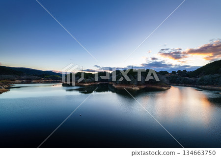 Evening view of Nara Nunome Dam in December, when there is a water shortage. Clouds remaining on the mountainside and a clear sunset sky. Evening view of Nara Nunome Dam in December, when there is a water shortage. Clouds remaining on the mountainside and a clear sunset sky. 134663750