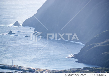 A passenger plane flying over the cliff-lined coastline of Hachijojima, a dynamic sky and seascape 134666887