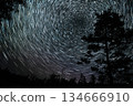 Star trails create mesmerizing patterns above a forest during a clear night sky 134666910