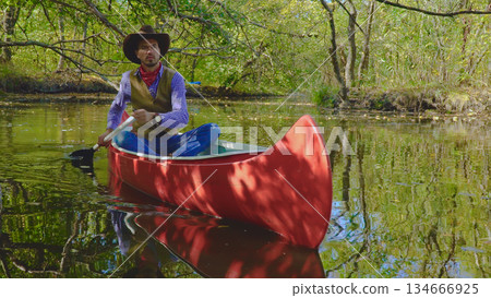 Cowboy in a canoe floats on the river in the forest Cowboy in a canoe floats on the river in the forest 134666925