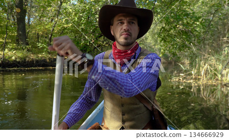 Cowboy in a canoe floats on the river in the forest Cowboy in a canoe floats on the river in the forest 134666929