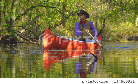 Cowboy in a canoe floats on the river in the forest Cowboy in a canoe floats on the river in the forest 134666931