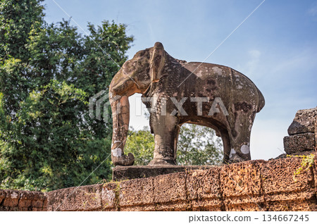 Side view of weathered stone elephant statue standing as guardian at ancient east mebon temple ruins in angkor wat complex Side view of weathered stone elephant statue standing as guardian at ancient east mebon temple ruins in angkor wat complex 134667245
