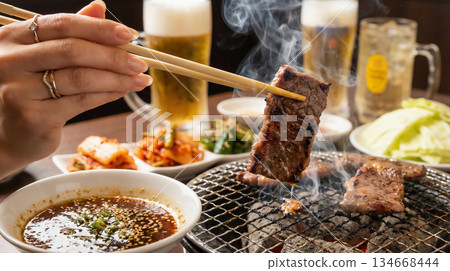 A man picking up hot charcoal-grilled meat with chopsticks and drinking beer 134668444