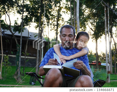 Father and Daughter Reading Book Together Outdoors in the Sunset Light. 134668871
