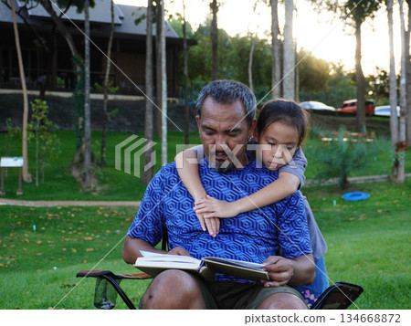 Father and Daughter Reading Book Together Outdoors in the Sunset Light. Father and Daughter Reading Book Together Outdoors in the Sunset Light. 134668872