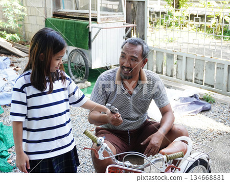 Father and Daughter Repairing a Bicycle Together, Learning Practical Skills. Father and Daughter Repairing a Bicycle Together, Learning Practical Skills. 134668881