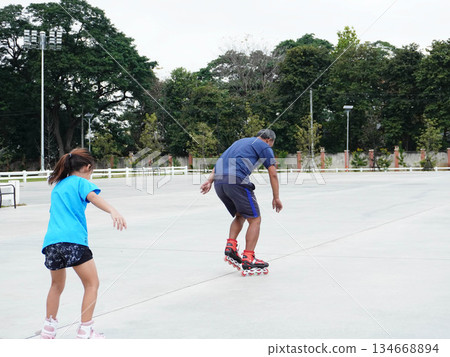 A father and daughter are roller skating together outdoors. A father and daughter are roller skating together outdoors. 134668894