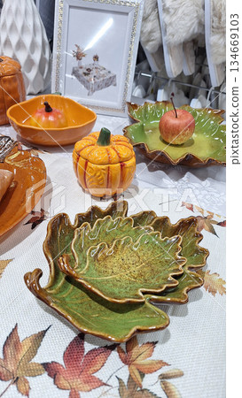 Artistic autumn-inspired ceramic dishes and pumpkin-shaped bowls displayed on a decorative table Artistic autumn-inspired ceramic dishes and pumpkin-shaped bowls displayed on a decorative table 134669103