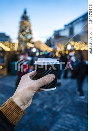 Hand Holding Hot mulled wine, Coffee, cocoa, tea, at Festive Christmas Market with Blurred Lights Hand Holding Hot mulled wine, Coffee, cocoa, tea, at Festive Christmas Market with Blurred Lights 134670498