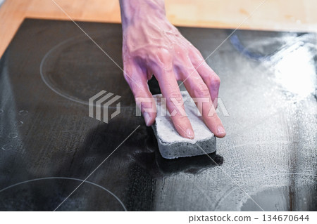 Hand cleaning ceramic cooktop with sponge in modern kitchen 134670644