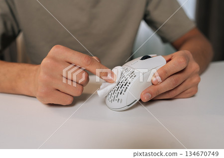 Close-up of person hands cleaning white wireless ergonomic computer mouse with small cleaning cloth, ensuring hygiene and proper maintenance of modern technology peripheral. Close-up of person hands cleaning white wireless ergonomic computer mouse with small cleaning cloth, ensuring hygiene and proper maintenance of modern technology peripheral. 134670749