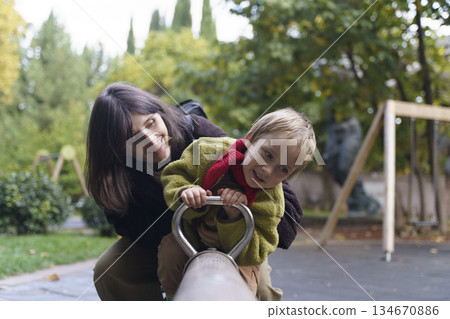 Happy Mother and Young Son Playing on Seesaw at Outdoor Playground 134670886
