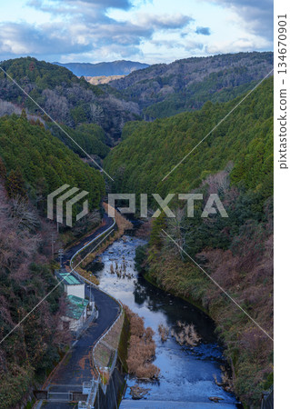 A December evening view of Nara Nunome Dam, where water is scarce. The lower reaches of the Nunome River, where leafless deciduous trees stand out, and the Kasagi mountain range bathed in the setting sun. 134670901