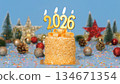 Happy New Year 2026, cute cake with golden ribbon with candle number 2026 for new year celebrate party was lit. decorate with Christmas ornament at blue background, horizontal 134671354