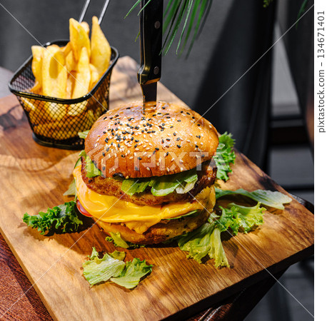 Delicious burger with fries served on wooden plate in modern restaurant Delicious burger with fries served on wooden plate in modern restaurant 134671401