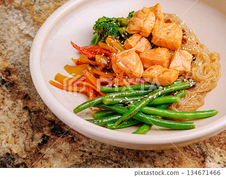 Salmon and vegetable stir fry served with noodles on a stone countertop 134671466
