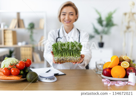 A nutritionist smiles while holding a tray of microgreens, surrounded by fresh fruits and vegetables, promoting healthy eating habits. A nutritionist smiles while holding a tray of microgreens, surrounded by fresh fruits and vegetables, promoting healthy eating habits. 134672021