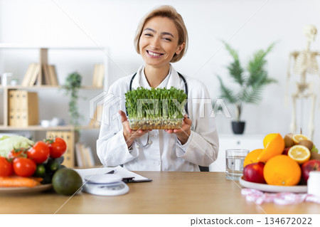 A smiling nutritionist holds a container of microgreens, surrounded by fresh fruits and vegetables, promoting healthy eating. A smiling nutritionist holds a container of microgreens, surrounded by fresh fruits and vegetables, promoting healthy eating. 134672022