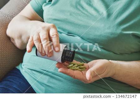 Older Female hands holding green herbal capsules from bottle 134672147