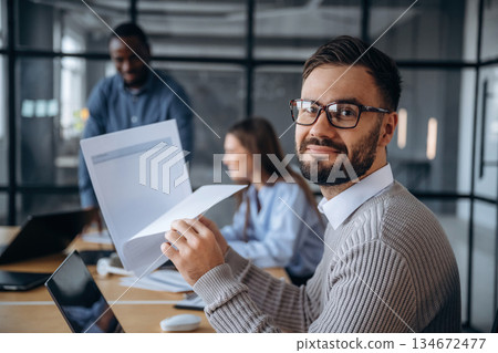 Documents in hands. Professional workers are in the modern office together Documents in hands. Professional workers are in the modern office together 134672477