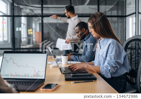 Man is standing by the glass, showing information. Professional workers are in the modern office together Man is standing by the glass, showing information. Professional workers are in the modern office together 134672986