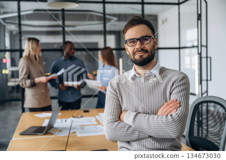Man is standing with arms crossed. Professional workers are in the modern office together 134673030