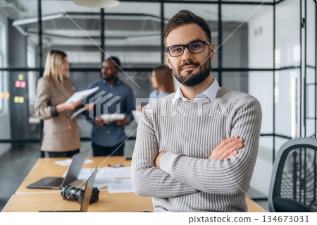 Man is standing with arms crossed. Professional workers are in the modern office together Man is standing with arms crossed. Professional workers are in the modern office together 134673031