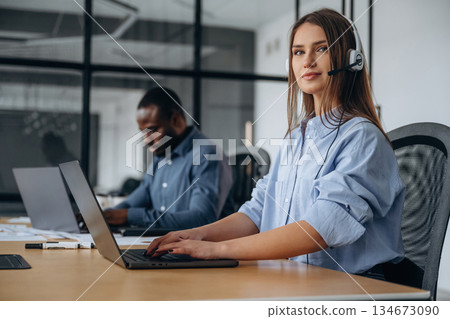 View from the side. People are working in the call center in headphones and laptops View from the side. People are working in the call center in headphones and laptops 134673090