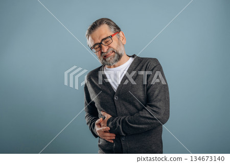 Pain in the right side. Senior man is standing in the studio against background 134673140