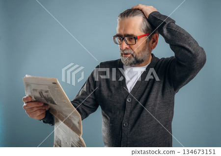 Reading the newspaper. Senior man is standing in the studio against background 134673151
