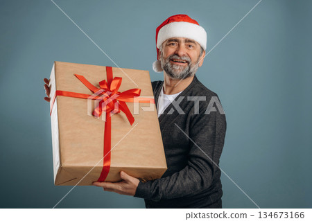 In Santa hat and with gift box. Senior man is standing in the studio against background 134673166