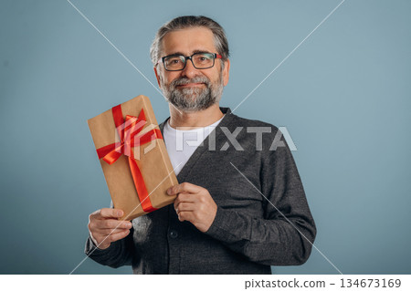 New year presents. Senior man is standing in the studio against background New year presents. Senior man is standing in the studio against background 134673169