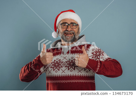 In Santa hat and with gift box. Senior man is standing in the studio against background In Santa hat and with gift box. Senior man is standing in the studio against background 134673170