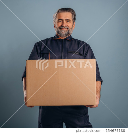 Delivery man is with box. Senior male is standing in the studio against background 134673188