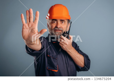Worker is talking by walkie talkie. Senior man is standing in the studio against background Worker is talking by walkie talkie. Senior man is standing in the studio against background 134673204