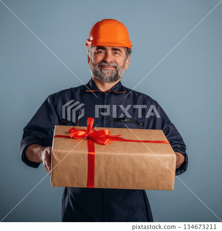 Here's Christmas present box. Senior man is standing in the studio against background Here's Christmas present box. Senior man is standing in the studio against background 134673211