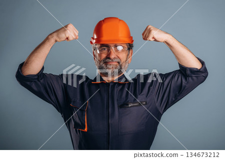 Strong, showing muscles, handyman. Senior man is standing in the studio against background 134673212