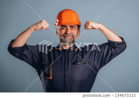 Strong, showing muscles, handyman. Senior man is standing in the studio against background 134673213
