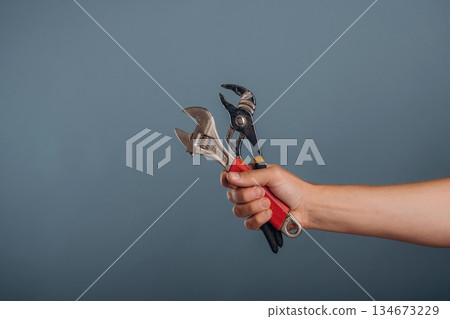 Man's hand holding professional pliers and wrench against background Man's hand holding professional pliers and wrench against background 134673229