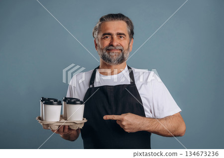Fresh drinks in hands of a waiter. Senior man is standing in the studio against background Fresh drinks in hands of a waiter. Senior man is standing in the studio against background 134673236