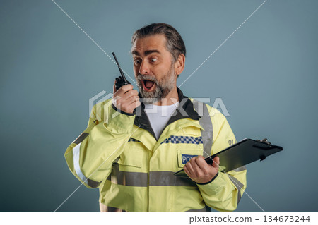 Construction worker is screaming into walkie talkie. Senior man is standing in the studio against background Construction worker is screaming into walkie talkie. Senior man is standing in the studio against background 134673244