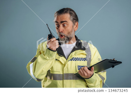 Construction worker is screaming into walkie talkie. Senior man is standing in the studio against background Construction worker is screaming into walkie talkie. Senior man is standing in the studio against background 134673245
