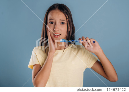 Pain in the tooth, holding toothbrush. Young girl is against background Pain in the tooth, holding toothbrush. Young girl is against background 134673422