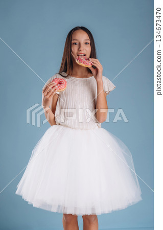 Two donuts in hands. Young girl in white dress is against background Two donuts in hands. Young girl in white dress is against background 134673470
