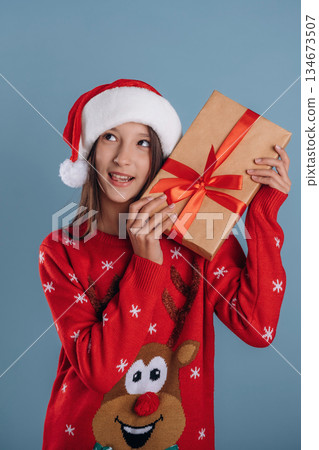 New year present gift box. Young girl in Christmas clothes is against background New year present gift box. Young girl in Christmas clothes is against background 134673507
