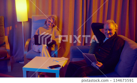 Elderly couple using laptop together at home with digital assistant support. 134673591